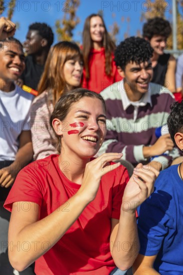 Young diverse friends and enthusiastic sports fans are cheering and clapping, showing excitement and support for their team while attending a live event in a stadium