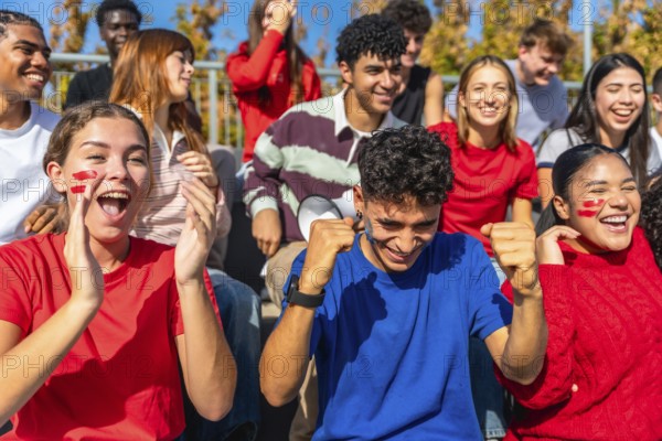 Energetic, diverse group of young adult spectators passionately cheering and celebrating their team's victory at a sports event in an outdoor stadium, showing excitement and unity