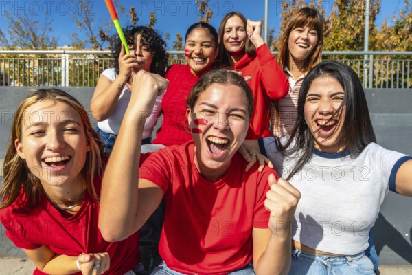 Diverse group of young women cheering loudly in a stadium, faces painted and fists raised, celebrating their team with joy, energy and friendship during a daytime game