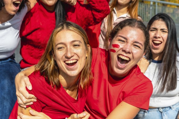 Group of excited young women wearing red shirts and face paint, screaming and cheering while watching a sports event together in a vibrant stadium atmosphere
