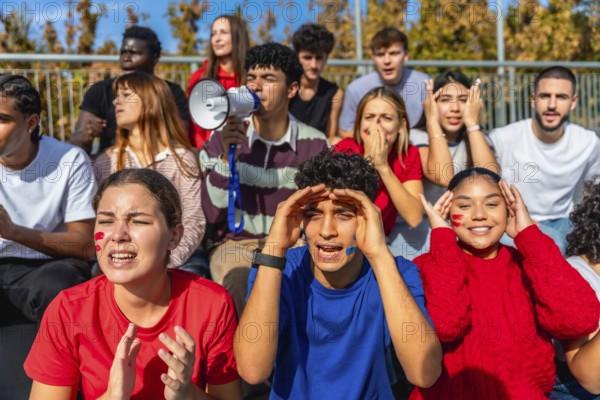 Group of diverse young sports fans cheering loudly, holding a megaphone, and showing a range of emotions from excitement and support to disappointment while watching a game at a stadium
