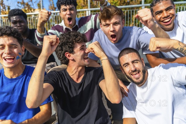 Group of excited young male sports fans from diverse backgrounds watching a match in a stadium, raising fists and shouting with joy, celebrating their team achieving success