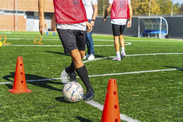 Football player practicing drills with ball and cones on artificial green turf, focused on improving skills, agility and control during outdoor training session