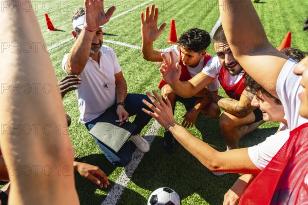 Soccer coach giving instructions and motivating his diverse team during a huddle on a green turf field, fostering teamwork, strategy, and unity before or during a game