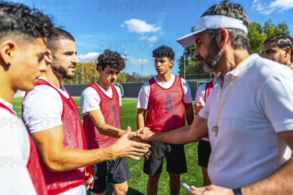 Soccer coach motivating and encouraging young male players with a handshake on a training field under a clear blue sky, fostering sportsmanship and teamwork