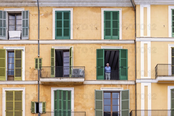 Senior citizen standing and looking out from open window in an old apartment building with balconies, Palma de Mallorca, Mallorca, Spain