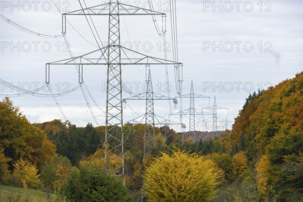 Power pylons in a vast landscape, surrounded by autumnal forests, changeable weather, beech, mixed forest, Swabian Alb biosphere reserve, Baden-Württemberg, Germany