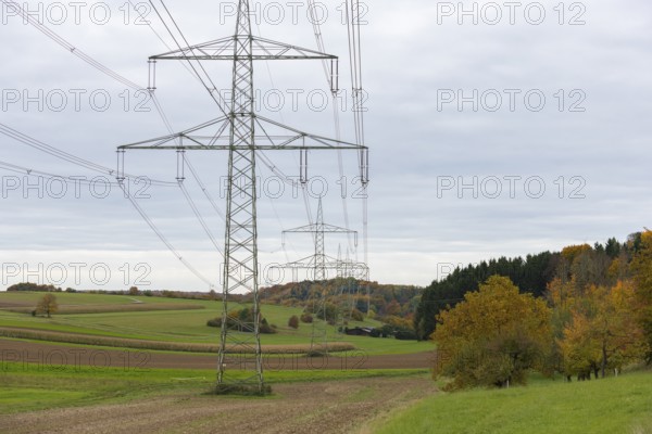 Power poles in a field under cloudy sky with autumn trees, Swabian Alps, Baden-Württemberg, Germany