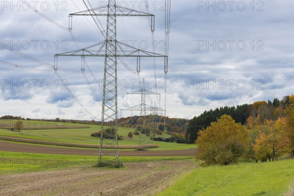 Power poles in a field under cloudy sky and autumn trees, Swabian Jura, Baden-Württemberg, Germany