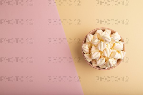 Orange and pink marshmallow in ceramic bowl on pink and orange pastel paper background, top view, flat lay, copy space, minimalism