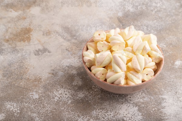 Orange and pink marshmallow in ceramic bowl on brown concrete background, side view, copy space, minimalism