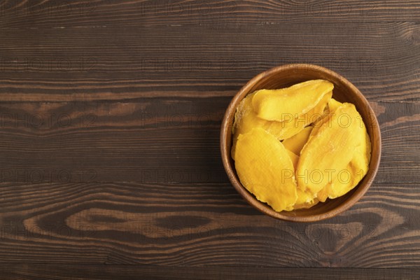 Dried Mango in wooden bowl on brown wooden background. Top view, copy space, flat lay. healthy food, minimalism