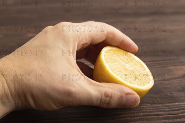 Yellow Lemon Cut in half with hand on brown wooden background. Side view, close up. healthy food, vegetable, minimalism. citrus