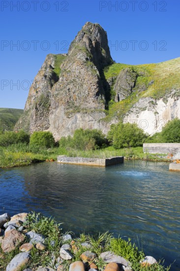 Clear water flows through a green landscape, framed by majestic, sunlit rocks, hot spring, Vorotan, Vorotan, Syunik province, Armenia