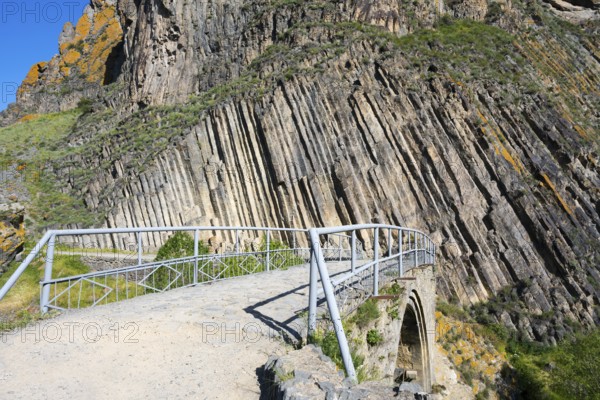 A narrow path with railing leads over a stone bridge, surrounded by unique vertical rock formations, Melik Tangi Bridge, behind it a basalt column formation, Vorotan River, Syunik Province, Armenia