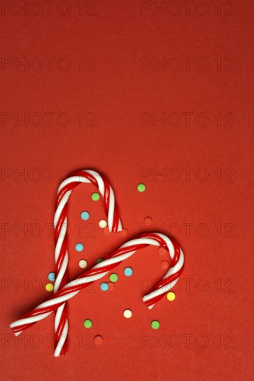 Candy canes and sugar confetti against red background, Christmas