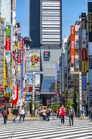 Bustling street scene in Japan with modern buildings and colorful billboards, figure of Godzilla head on a high-rise building, Shinjuku City, Tokyo, Japan