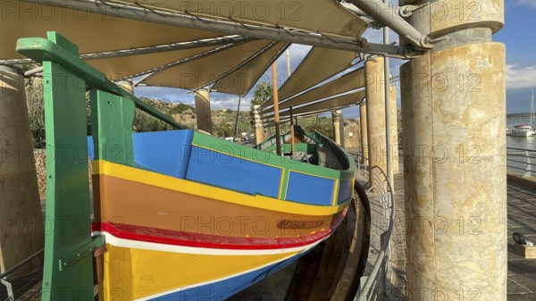Monument to traditional fishing boats abandoned jacked up typical colorful painted old fishing boat with large rudder blade at the stern of Gozo at Gozo harbour, Mgarr Harbour, Gozo, Malta