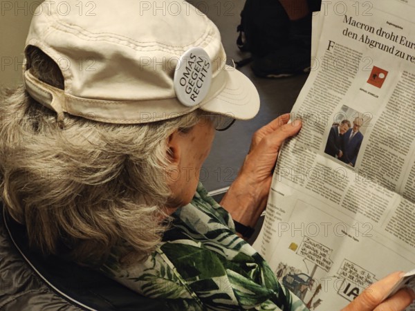 Elderly woman reading in the newspaper with a sticker on her cap from the cross-party citizens' initiative Omas gegen Rechts, Essen, Germany