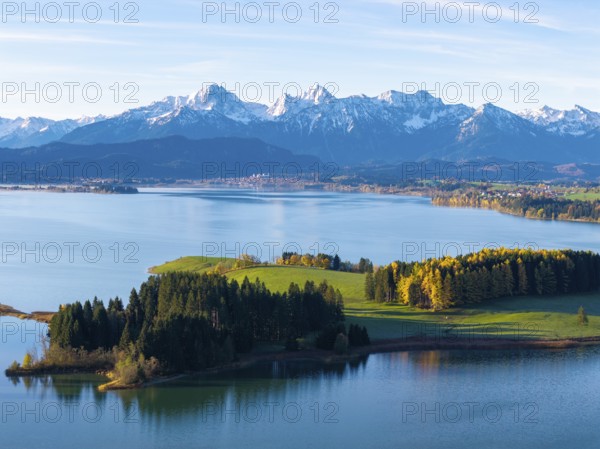 Idyllic mountain landscape with a calm lake, green hills and golden autumn trees under a blue sky