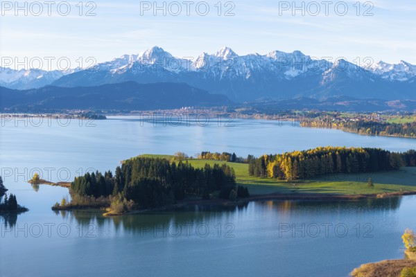 Picturesque landscape with a calm lake and autumn-colored trees against an alpine backdrop in the background