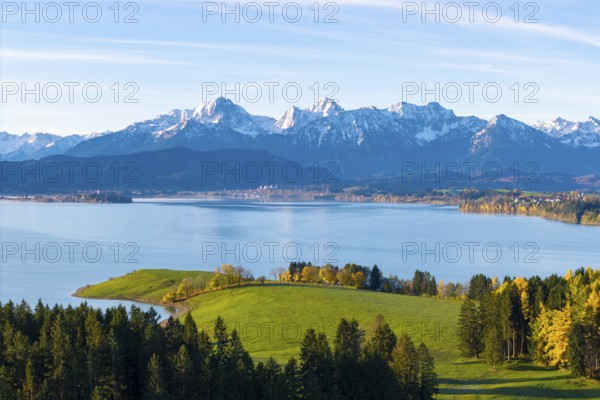 Extensive alpine landscape with a quiet lake surface and autumn-colored trees under a clear sky