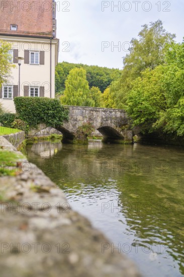 An old stone bridge over a quiet river flanked by buildings and trees, ZFP Zwiefalten, Reutlingen district, Germany