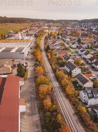 A Hermann Hesse Railway line runs through a town with autumn leaves, surrounded by residential buildings and an industrial area, Althengstett, Calw district, Germany