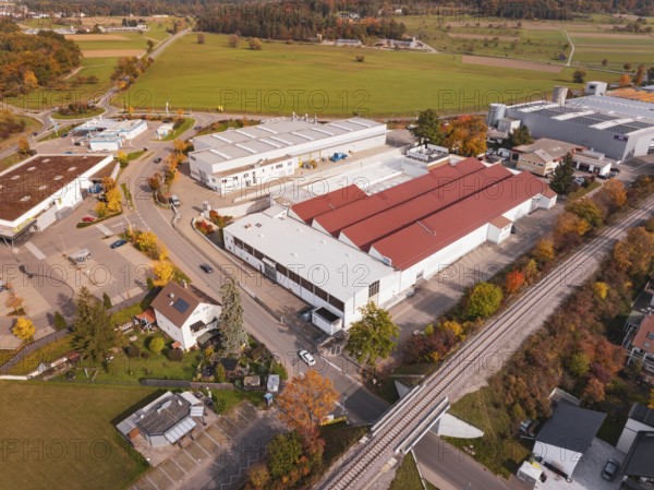 An industrial complex with red roofs and a railroad line, surrounded by autumn trees, Althengstett, Calw district, Germany