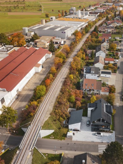 A railway line that runs through an autumn landscape with houses and industrial buildings, Althengstett, Calw district, Germany