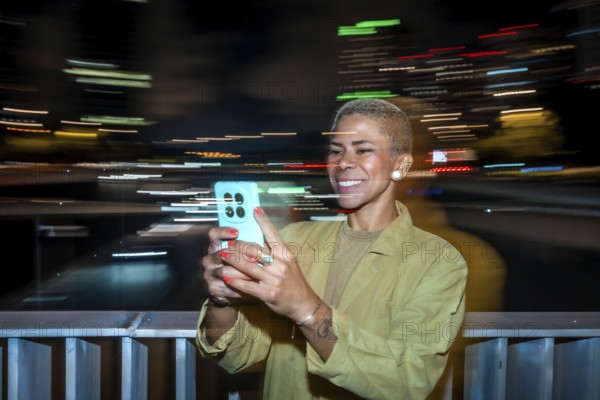 Smiling woman taking a video or picture with a smartphone, capturing the blurred light trails of a busy city at night on a bridge, representing modern technology and urban life