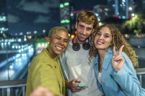 Group of diverse friends smiling and posing for a selfie at night, celebrating friendship and youth with city lights creating a vibrant urban background