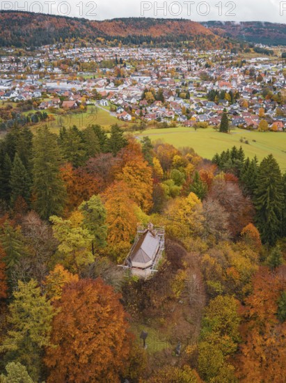 Small pavilion in a colorful autumn forest with a view of a city in the distance under cloudy sky, Wehingen, Tuttlingen district, Germany