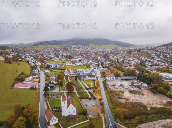 Aerial view of a village with church surrounded by fields, roads and wooded hills under a thick cloud cover, Wehingen, Tuttlingen district, Germany