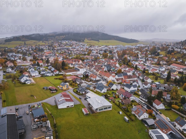 View of a city with colorful roofs surrounded by green fields and wooded hills under gray clouds, Wehingen, Tuttlingen district, Germany