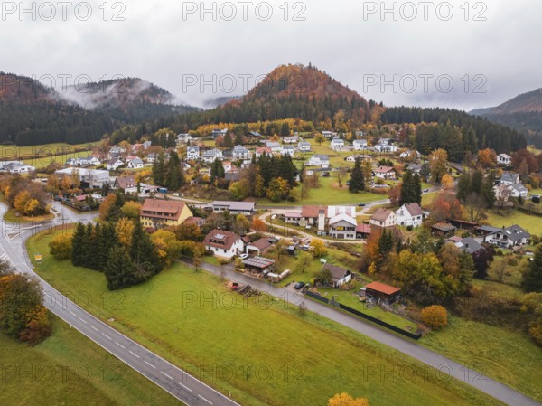Village nestled in autumnal hills with colorful trees and a curved road, Wehingen, Tuttlingen district, Germany