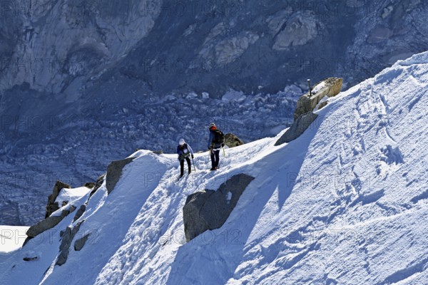 Two ascended mountaineers run across a snow-covered mountain ridge, Aiguille du Midi, Chamonix-Mont-Blanc, Haute-Savoie, France