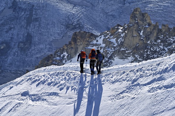 Three ascended mountaineers run across a snow-covered mountain ridge, Aiguille du Midi, Chamonix-Mont-Blanc, Haute-Savoie, France