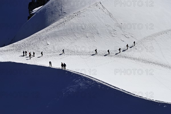 A group of mountaineers runs across a snow-covered mountain, Aiguille du Midi, Chamonix-Mont-Blanc, Haute-Savoie, France
