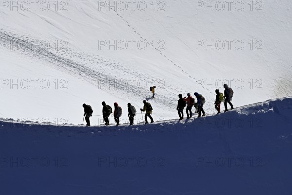 A group of mountaineers runs across a snow-covered mountain ridge, Aiguille du Midi, Chamonix-Mont-Blanc, Haute-Savoie, France