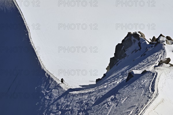 A mountaineer climbs over a snow-covered mountain ridge, Aiguille du Midi, Chamonix-Mont-Blanc, Haute-Savoie, France