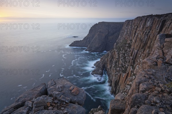 Long exposure shows sunset over the cliffs of Cape Raoul. Golden light hits the sea and colors the rocks warmly in the evening. Cape Raoul, Tasman Peninsula, Tasmania, Australia