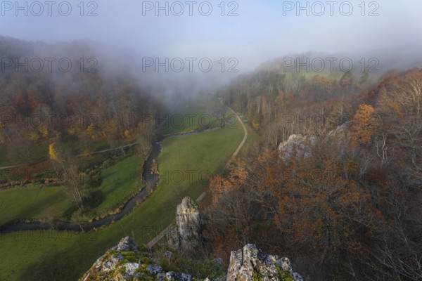 Autumn landscape with rising fog over the Grosse Lauter river loop in Lautertal at sunrise. View from above of the picturesque valley with colorful deciduous forest and rolling hills, Großes Lautertal, Baden-Württemberg, Germany