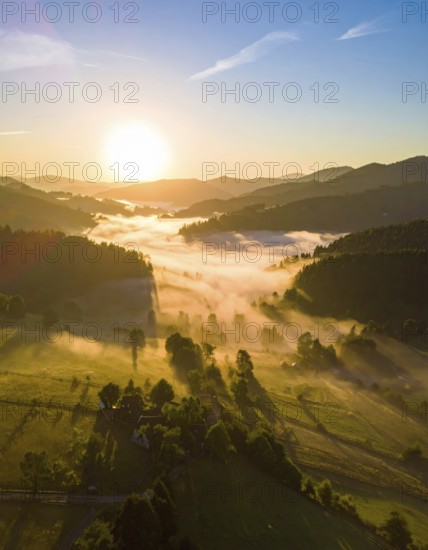 Sunrise over a fog covered village in a rural landscape, golden morning light, serene autumn atmosphere, hills and mountains in the background, AI generated