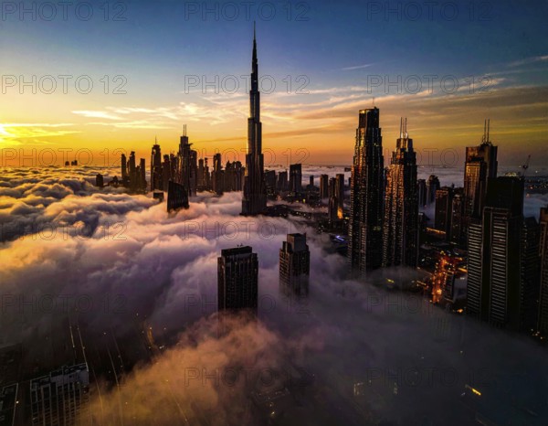 City scape emerging from a dense enveloping fog in sunrise and skyscrapers piercing the haze, big metropolis with skyline, mist on ground, blue sky, city in an aerial view, AI generated