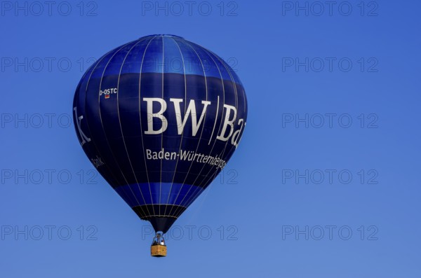 A hot air balloon, registration D-OSTC, rises into the air as part of an air show at the Rossfeld Air Sports Association's Flying Festival on Rossfeld in Metzingen-Glems, Baden-Württemberg, Germany, for editorial use only