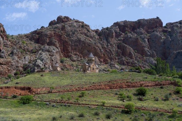 Church on green meadow against dramatic rocky backdrop under blue sky, Noravank monastery, Surb Astvatsatsin mausoleum church and Surb Karapet baptism church, Noravank, Vayots Dzor province, Wajoz Dzor, Armenia, Caucasus