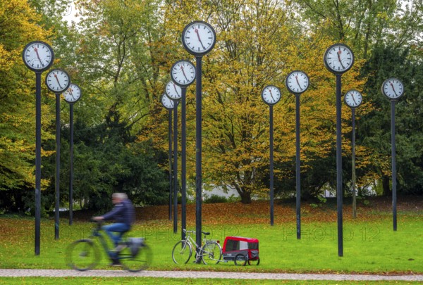 The art installation Zeitfeld in Volksgarten Park in Düsseldorf-Oberbilk, a total of 24 station clocks, on 6 meter high steel columns, have been running synchronously since 1987, cyclists in the municipal park, artwork by Düsseldorf artist Klaus Rinke, symbol of time, time change, North Rhine-Westphalia, Germany