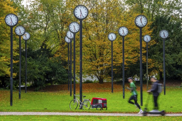 The art installation Zeitfeld in Volksgarten Park in Düsseldorf-Oberbilk, a total of 24 station clocks, on 6 meter high steel columns, have been running synchronously since 1987, jogger in the municipal park, artwork by Düsseldorf artist Klaus Rinke, symbol of time, time change, North Rhine-Westphalia, Germany