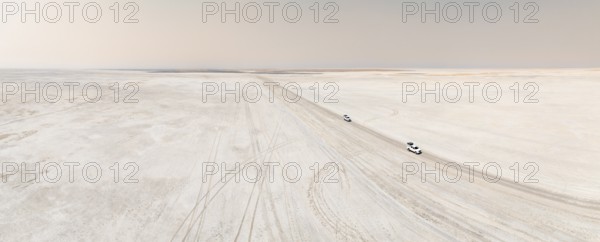 Aerial view, two off-road cars driving on a salt pan, arid landscape, Botswana